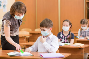 Eine Lehrerin und einzelne Schüler mit Masken in einer Schulklasse.