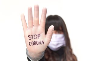 Eine Frau mit Alltagsmaske steckt die rechte Hand mit dem Text "Stop Corona" entgegen.