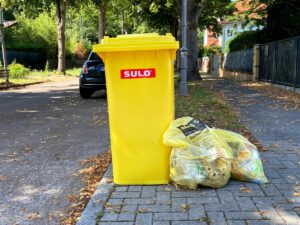 Ein Gelber Sack und eine Gelbe Tonne am Straßenrand.