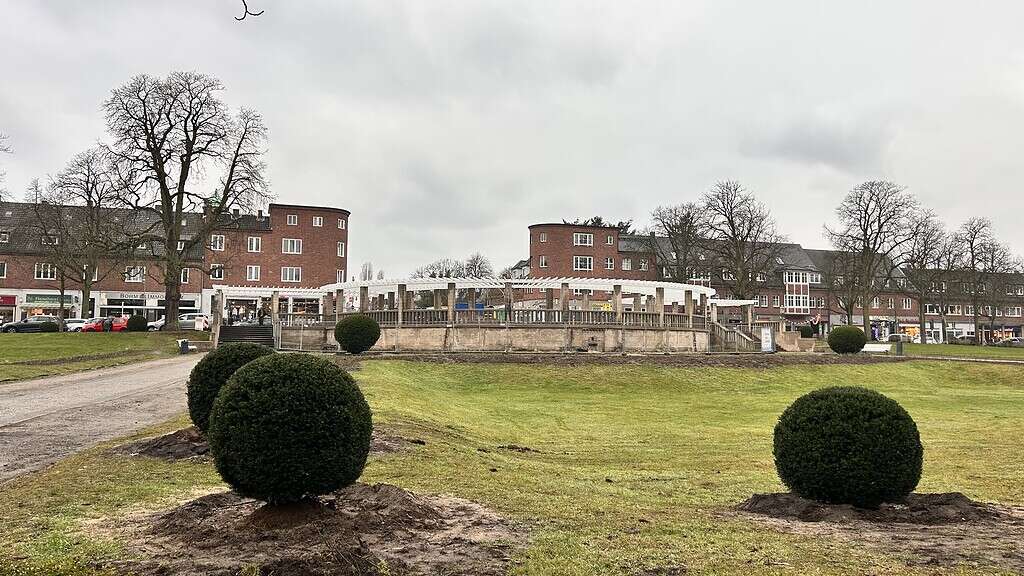 Zeltinger Paltz in Frohnau mit kugelförmig geschnittenen Büschen im Vordergrund, dahinter die Pergola und Gebäude im Hintergrund an einem bewölkten Tag.