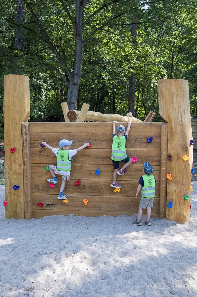 Kinder klettern an einer Holzwand mit bunten Klettergriffen