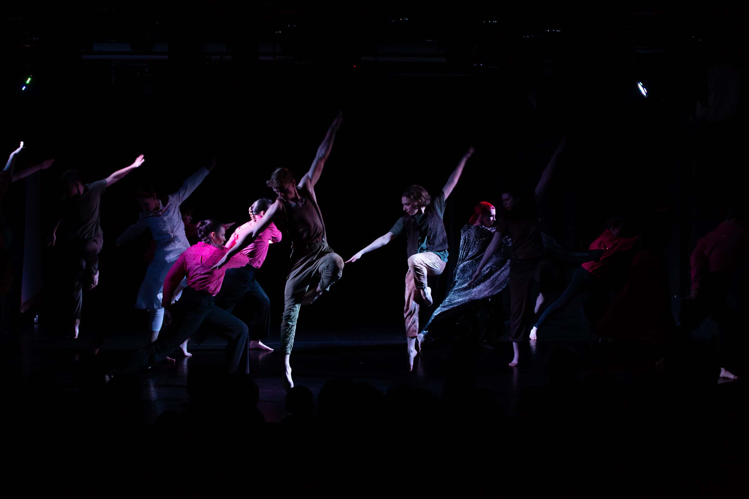 Junge Tänzerinnen und Tänzer der Young Trybe Dance Company in bunten Kostümen bei einer Aufführung auf dunkler Bühne.