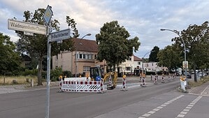 Straßenschild Waidmannsluster Damm Ecke Im Brachfeldwinkel, dahinter Absperrbaken und ein Bagger auf der Fahrbahn