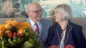 Ein älteres Ehepaar sitzt lächelnd nebeneinander, davor ein Blumenstrauß und eine dekorative Zahl 60.