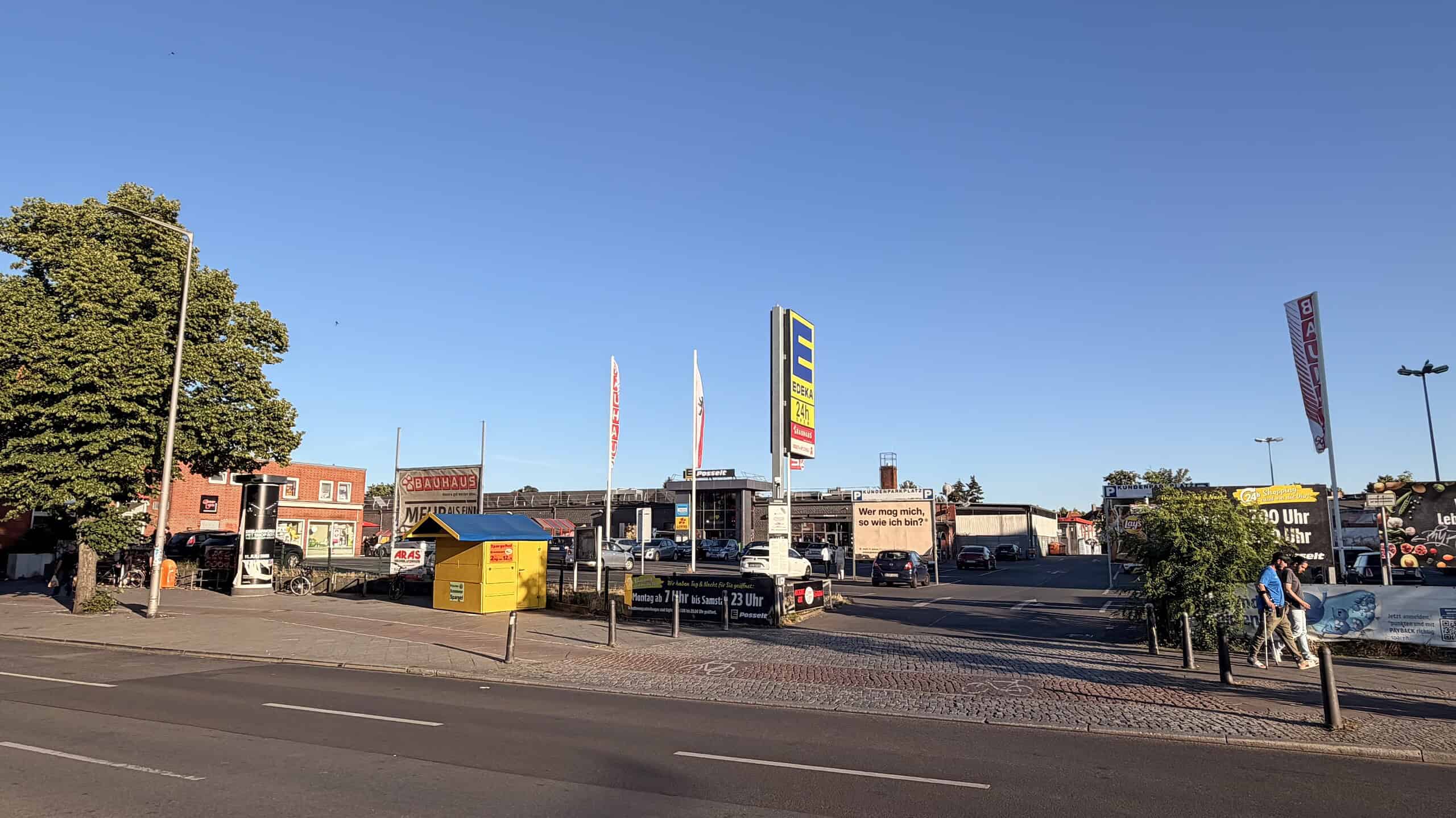 Blick von der Straße auf den EDEKA-Parkplatz am U-Bahnhof Wittenau mit Supermarkt, Werbetafeln und parkenden Autos.