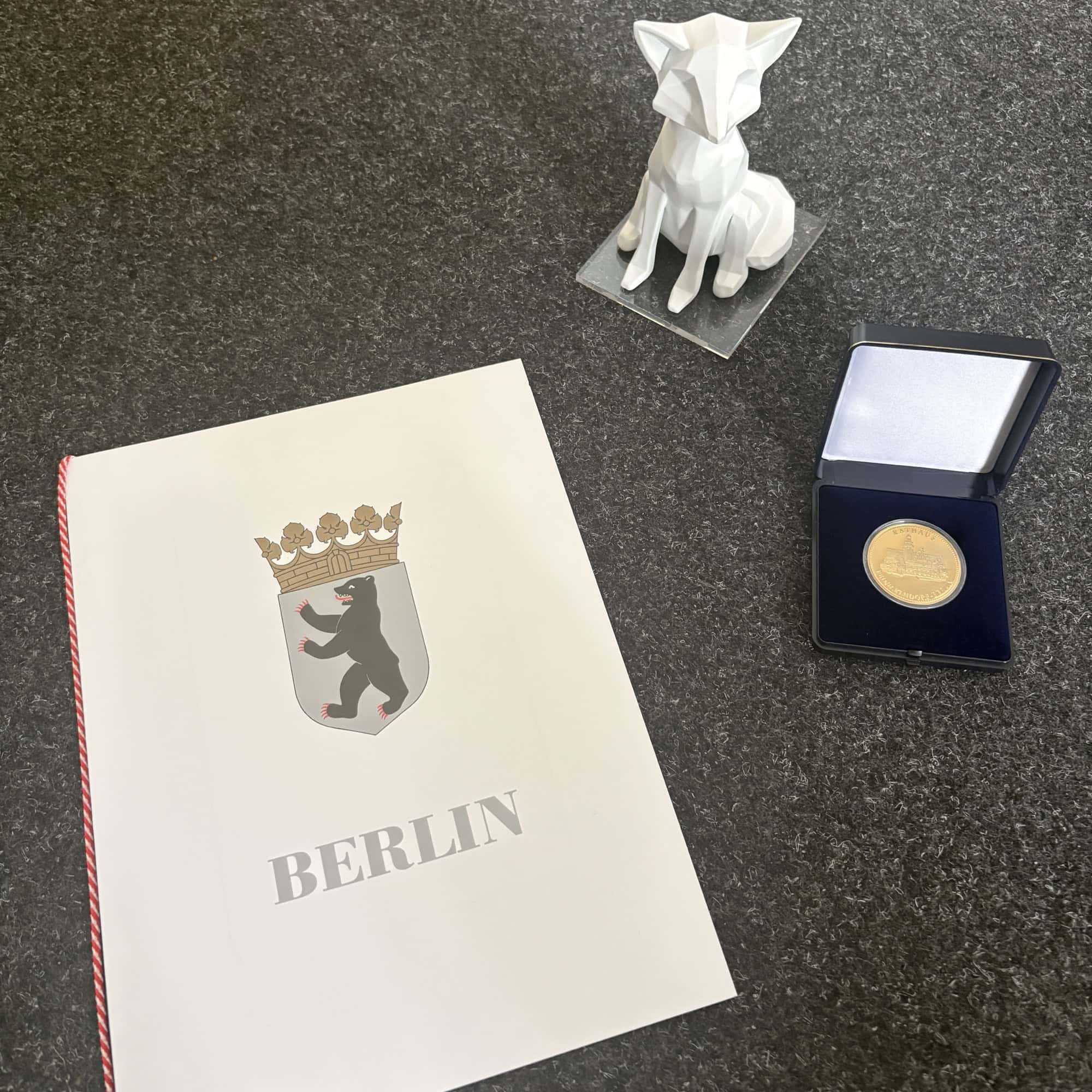 Reinickendorfer Medaille im Etui, weiße Fuchs-Miniaturskulptur und Urkundenmappe mit dem Berliner Bärenwappen