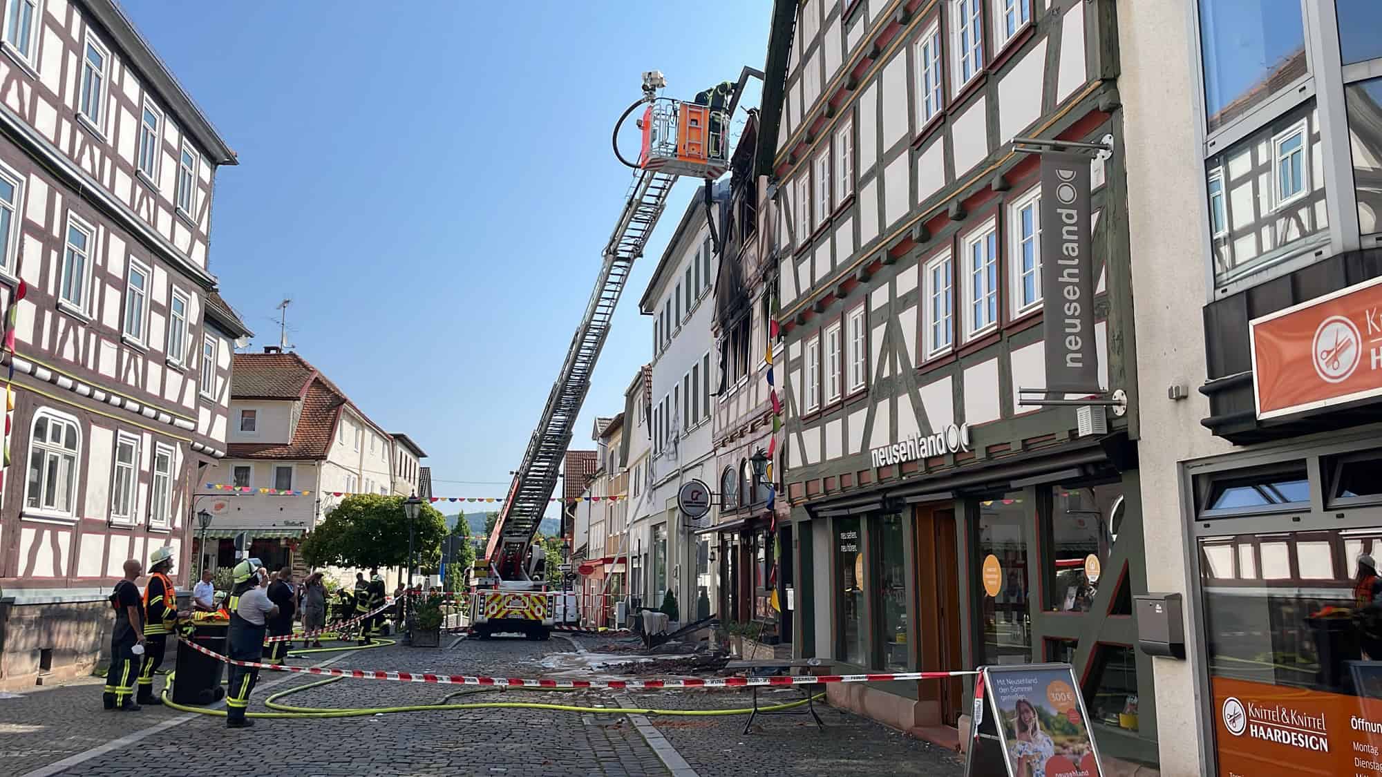 Eine ausgefahrene Drehleiter der Feuerwehr steht in einer engen Altstadtgasse zwischen Fachwerkhäusern, im Vordergrund liegen Schläuche auf dem Pflaster, Feuerwehrleute stehen am Absperrband.