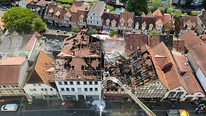 Luftaufnahme der Lauterbacher Altstadt: Mehrere aneinandergebaute Häuser sind bis auf das verkohlte Dachgebälk ausgebrannt, ringsum stehen unbeschädigte Fachwerkhäuser mit roten Ziegeldächern.