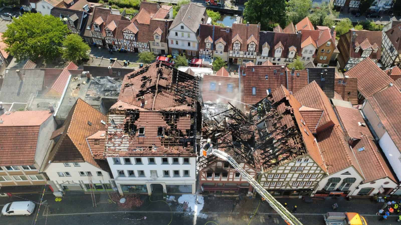 Luftaufnahme der Lauterbacher Altstadt: Mehrere aneinandergebaute Häuser sind bis auf das verkohlte Dachgebälk ausgebrannt, ringsum stehen unbeschädigte Fachwerkhäuser mit roten Ziegeldächern.