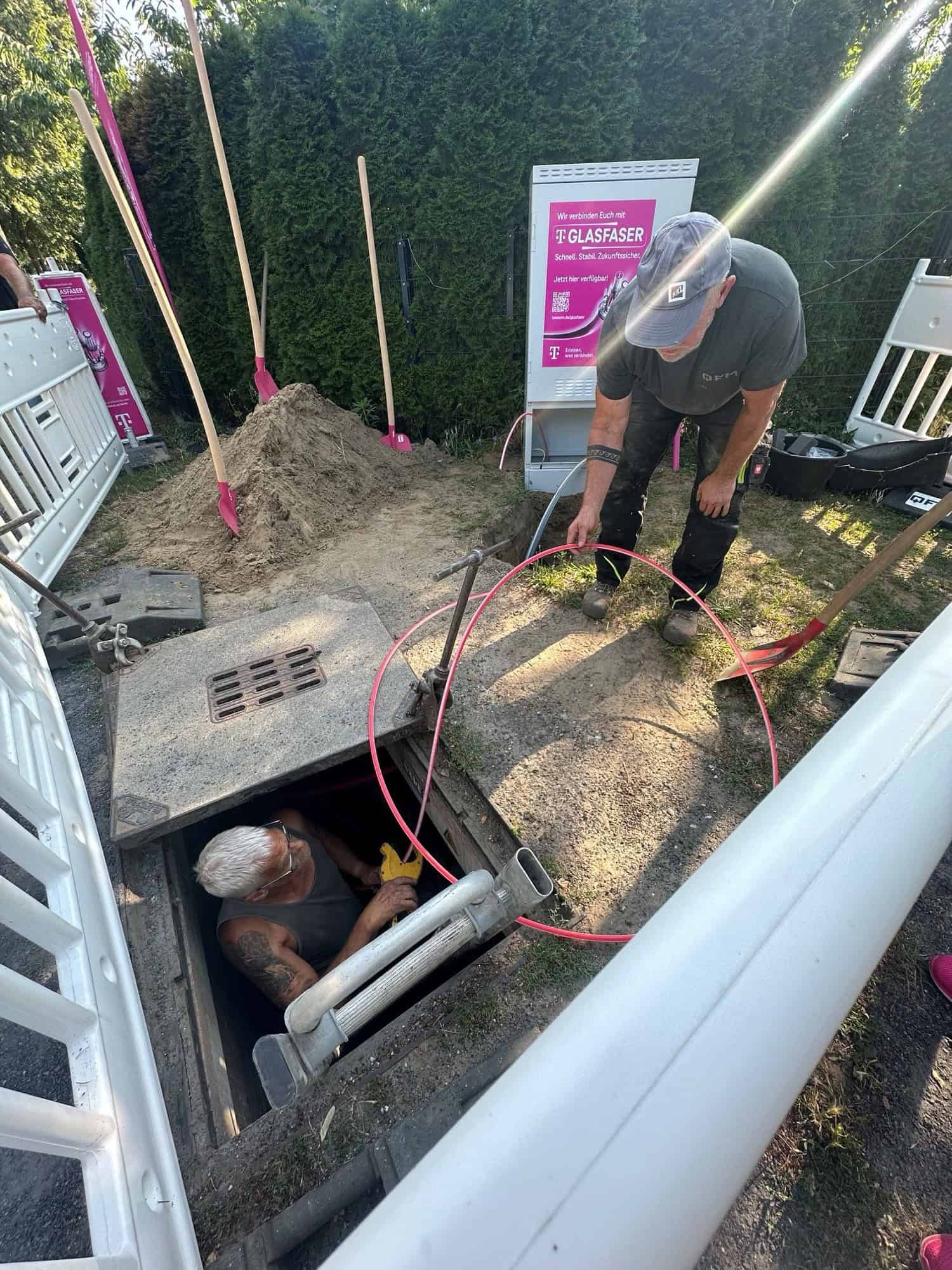 Bauarbeiter verlegen Glasfaserleitungen in einem Schacht