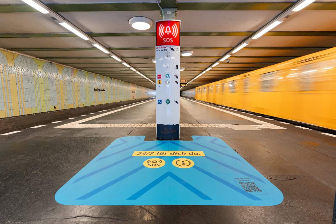 Hellblaue Pink*Zone-Markierung am U-Bahnhof Kurfürstenstraße, im Hintergrund fährt eine gelbe U-Bahn ein