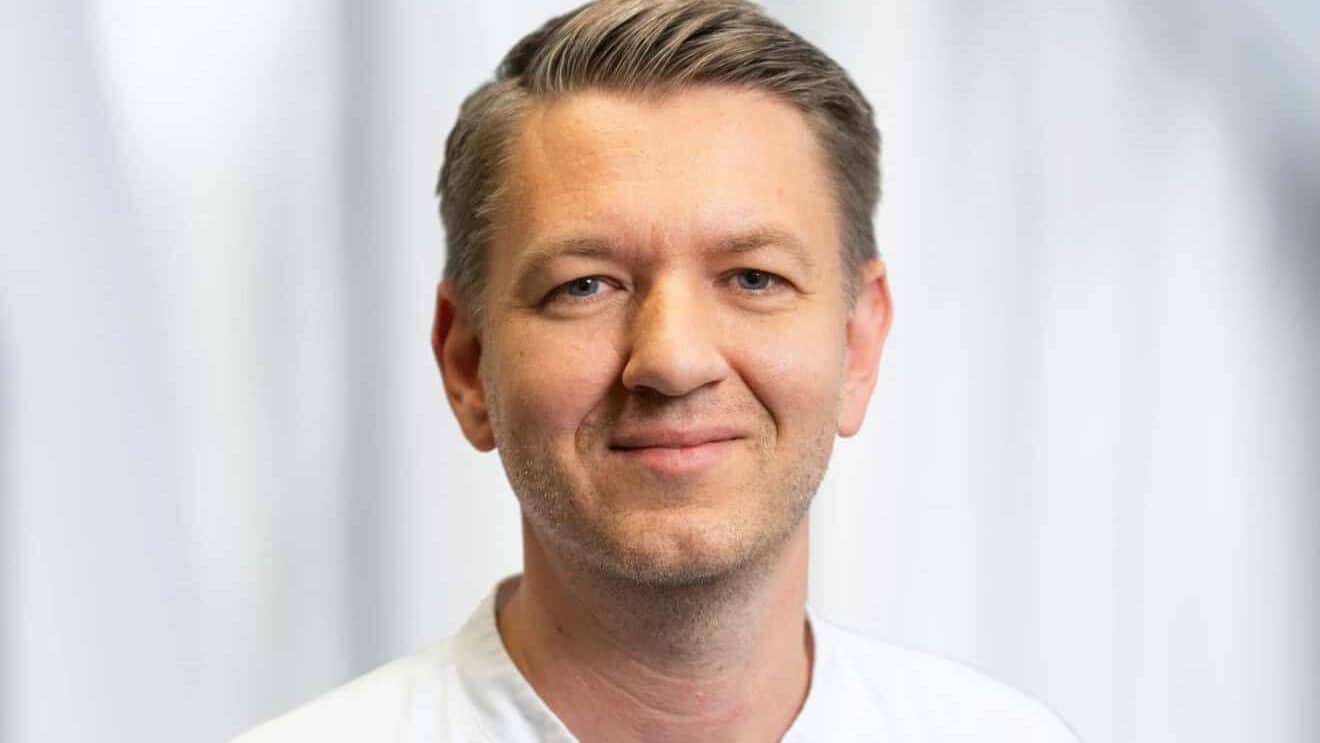 Porträt von Dr. med. Robert Steinicke im weißen Arztkittel über blauer Kasackjacke vor einem hellen, unscharfen Hintergrund.
