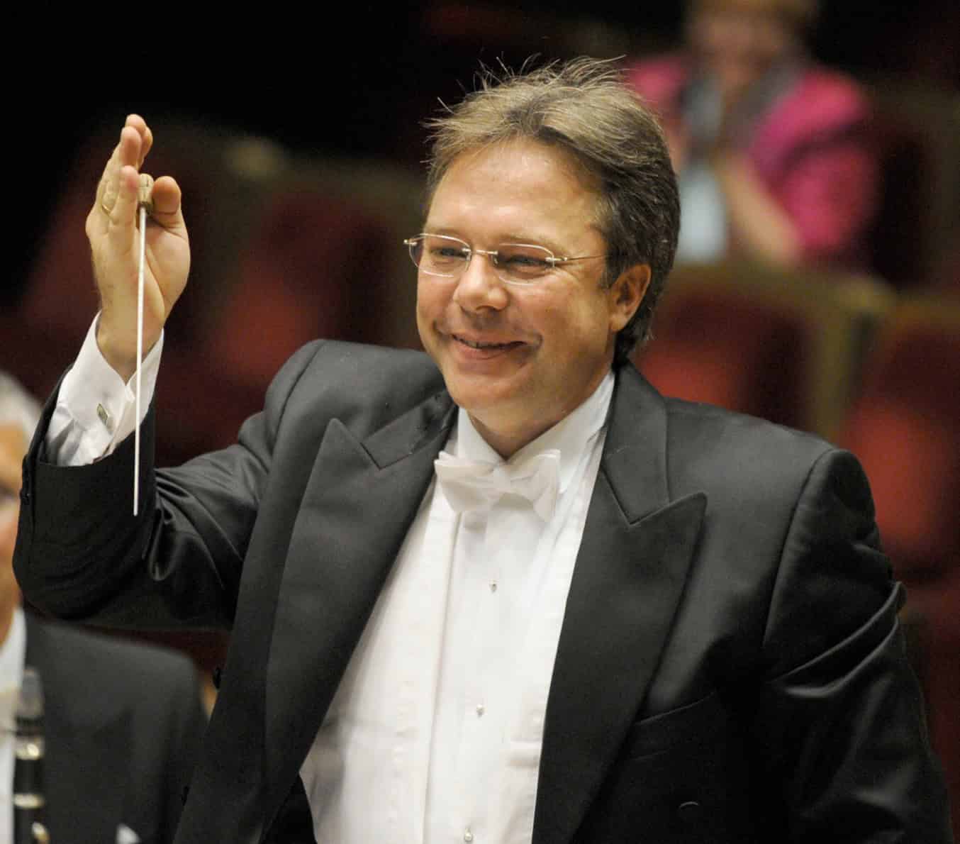 Prof. Thomas Clamor im Frack hebt lächelnd den Taktstock vor einem Orchester