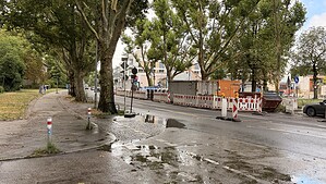 Wasserlache auf Gehweg und Fahrbahnrand an der Kreuzung Roedernallee und Fräsersteig in Berlin-Reinickendorf, im Hintergrund eine Baustellenabsperrung.