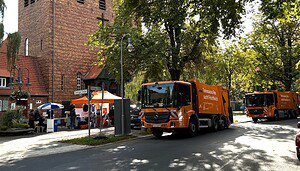 Zwei orange BSR-Fahrzeuge stehen an einer Straße neben einem Stand mit orangefarbenem Pavillon.
