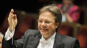 Prof. Thomas Clamor im Frack hebt lächelnd den Taktstock vor einem Orchester