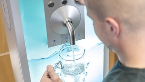 Ein Mann füllt an einem Wandwasserspender ein Glas mit sprudelndem Trinkwasser