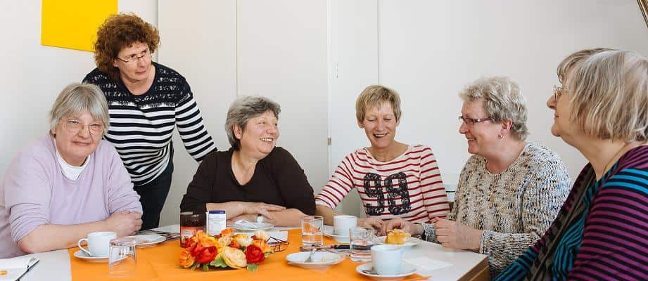 Frauen sitzen um einen Tisch bei Kaffee und Kuchen und sind angeregt ins Gespräch vertieft.