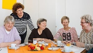 Frauen sitzen um einen Tisch bei Kaffee und Kuchen und sind angeregt ins Gespräch vertieft.