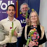 Fünf Mitglieder des Reinickendorfer Volt-Teams stehen mit Tulpen in der Hand vor einem violetten Volt-Banner, eine Frau hält ein Baby auf dem Arm.
