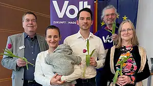Fünf Mitglieder des Reinickendorfer Volt-Teams stehen mit Tulpen in der Hand vor einem violetten Volt-Banner, eine Frau hält ein Baby auf dem Arm.