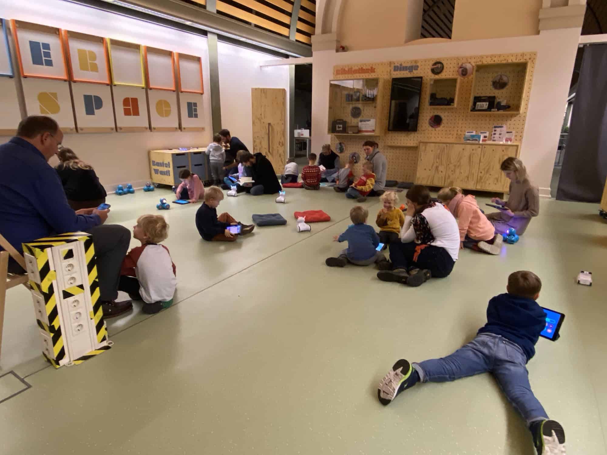 Kinder sitzen mit Tablets und kleinen Robotern auf dem Boden des Makerspace der Humboldt-Bibliothek.