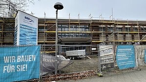 Das eingerüstete Paracelsus-Bad steht hinter einem Bauzaun, davor hängen blaue Banner der Berliner Bäder-Betriebe mit der Aufschrift „Wir bauen für Sie!“.