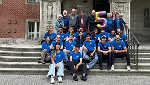 Gruppenbild mit 17 Jugendlichen in blauen T-Shirts und Erwachsenen auf einer Rathaustreppe, in der Mitte ein Luftballon in Form einer Fünf