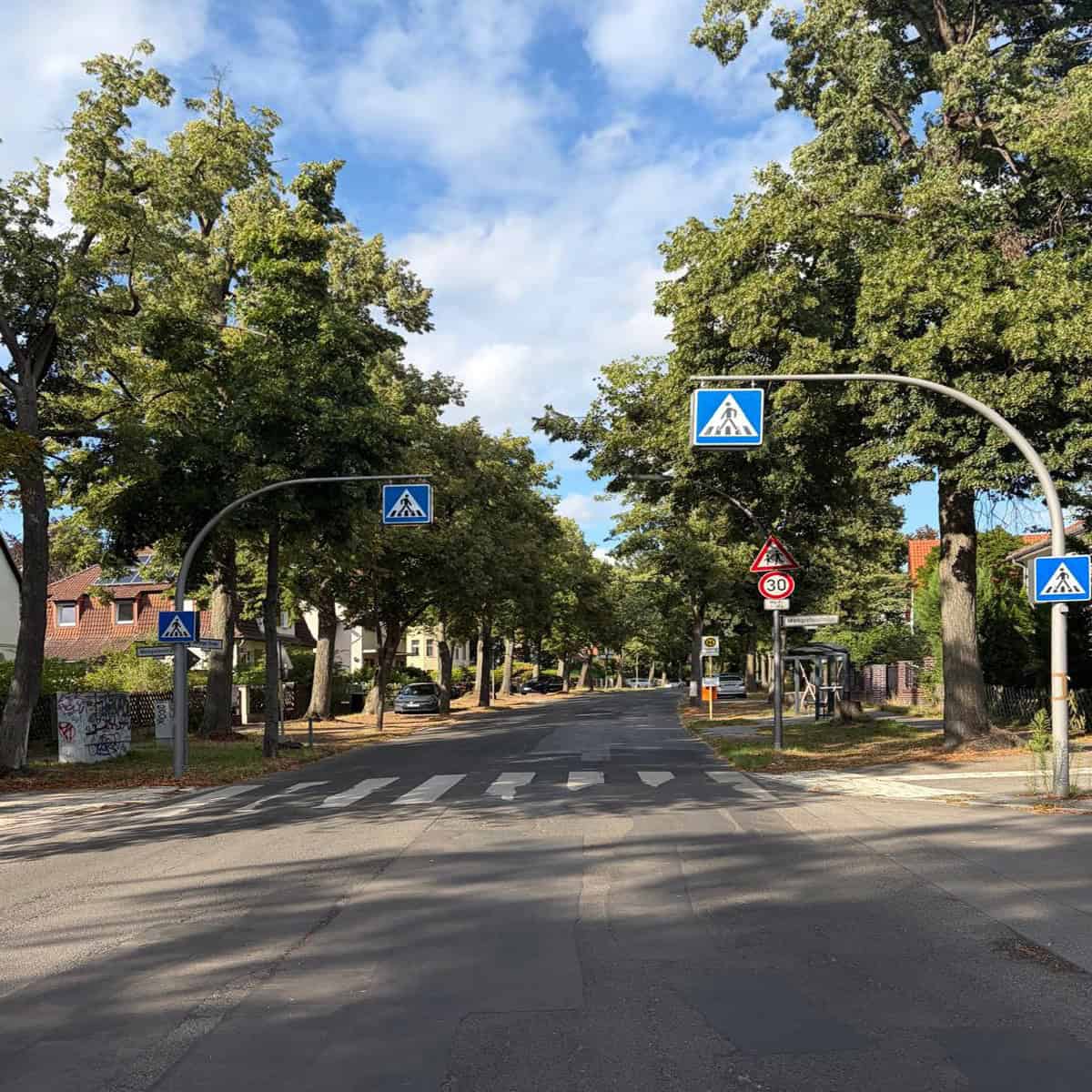 Zeltinger Straße an der Kreuzung Markgrafenstraße mit geflicktem Asphalt, Zebrastreifen und Bushaltestelle