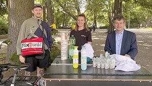 Zwei Mitarbeitende von Fixpunkt e. V. und Gesundheitsstadtrat Uwe Brockhausen stehen an einem Lastenrad mit Trinkflaschen, Bechern, Sonnencreme und Sonnenhüten unter Bäumen am Schäfersee.