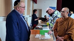 Auf einer Bühne mit rotem Vorhang sitzen fünf Personen nebeneinander auf Stühlen, eine Frau links moderiert, einer der Männer spricht in ein Mikrofon.