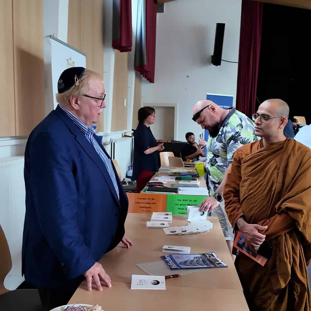 Auf einer Bühne mit rotem Vorhang sitzen fünf Personen nebeneinander auf Stühlen, eine Frau links moderiert, einer der Männer spricht in ein Mikrofon.