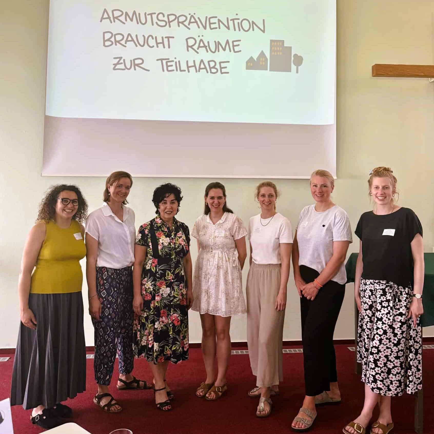 Sieben Frauen stehen nebeneinander vor einer Leinwand mit der Aufschrift Armutsprävention braucht Räume zur Teilhabe.