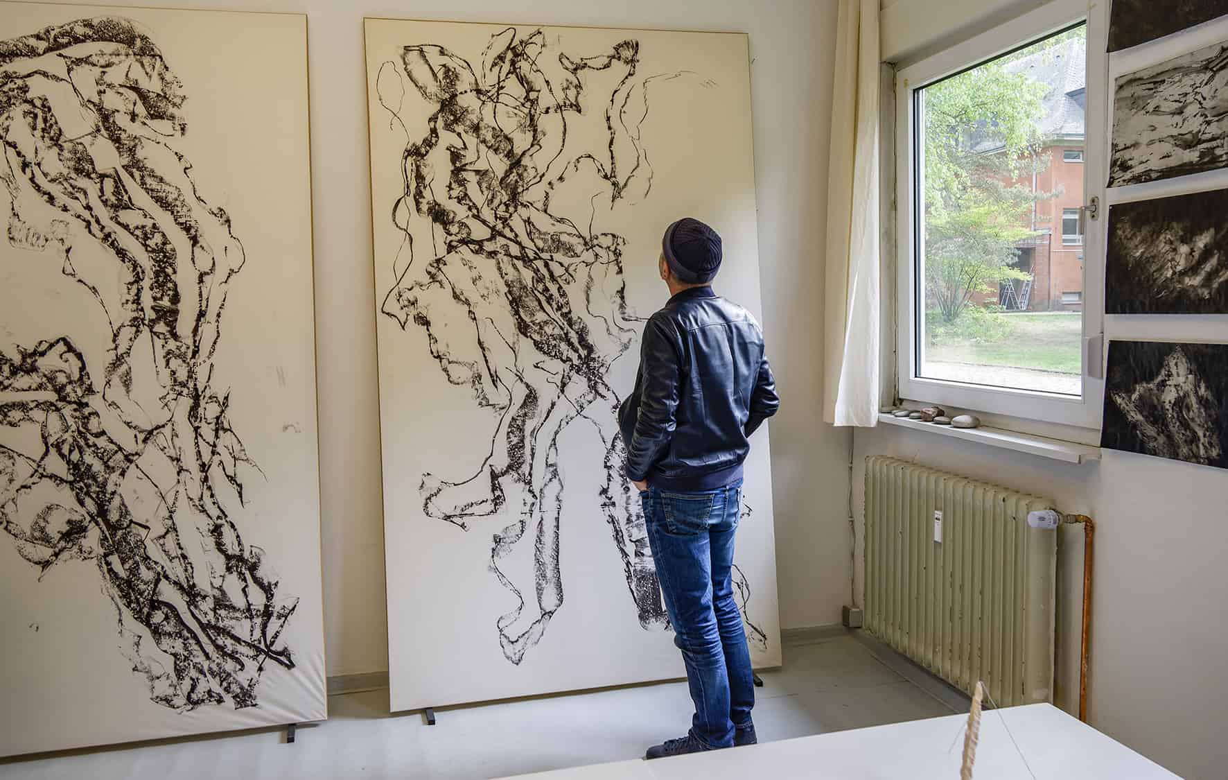 Ein Besucher steht vor zwei großformatigen schwarz-weißen Zeichnungen in einem Atelier