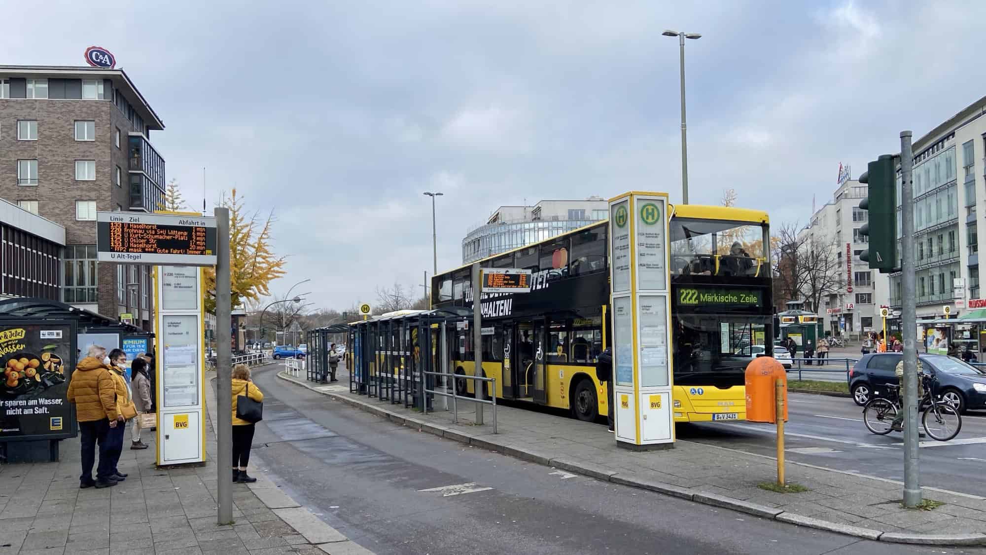 Ein gelber Doppeldeckerbus der BVG-Linie 222 mit dem Fahrtziel Märkische Zelle hält an der Haltestelle U Alt-Tegel, davor warten Fahrgäste am Fahrgastunterstand.
