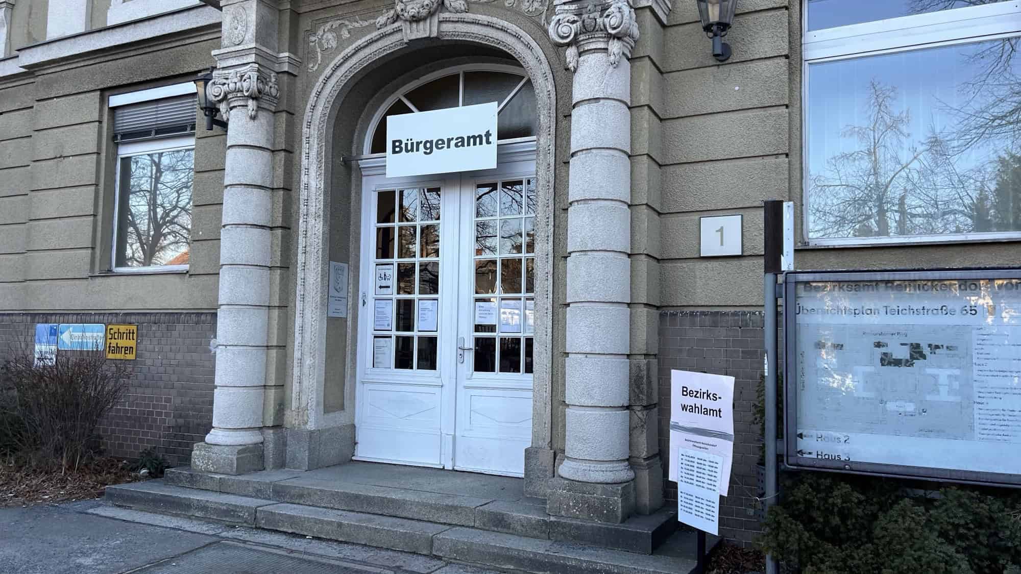 Eingang des Bürgeramts Reinickendorf-Ost in der Teichstraße 65 mit dem Schild Bürgeramt über der Tür und einem Aushang des Bezirkswahlamts daneben.