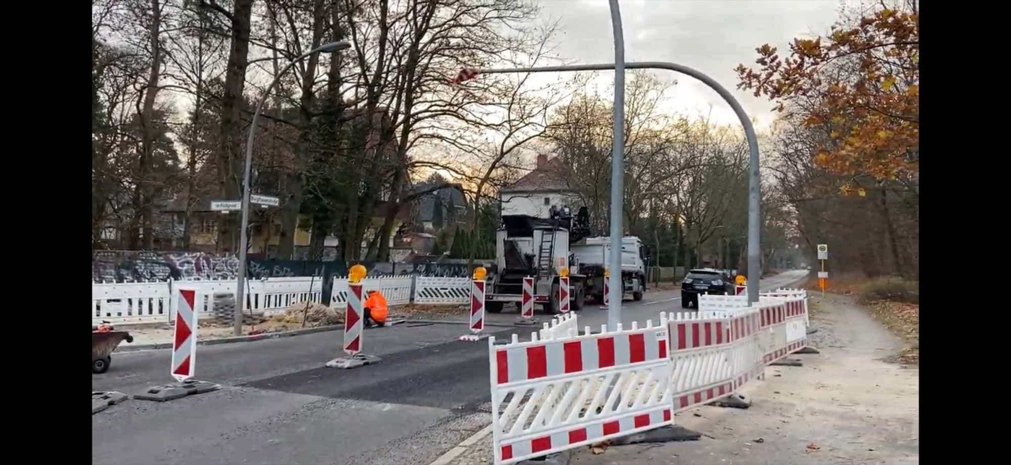 Rot-weiße Absperrgitter, ein Baufahrzeug und frisch asphaltierte Fahrbahn auf der Burgfrauenstraße in Berlin-Frohnau
