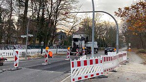 Rot-weiße Absperrgitter, ein Baufahrzeug und frisch asphaltierte Fahrbahn auf der Burgfrauenstraße in Berlin-Frohnau