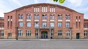 Symmetrische Backsteinfassade des Landesarchivs Berlin am Eichborndamm mit geschwungenem Dachabschluss und gläsernem Vordach über dem Eingang.
