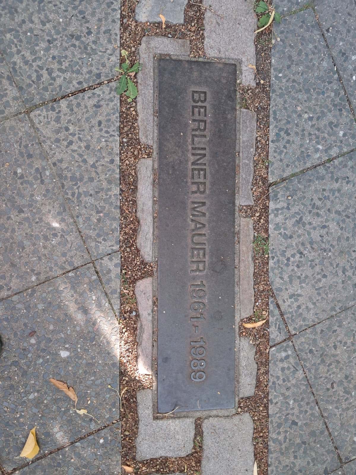 Eine in den Gehweg eingelassene Metallplatte mit der Aufschrift Berliner Mauer 1961-1989.
