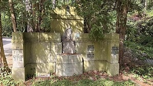 Steinerne Grabanlage aus Muschelkalk zwischen hohen Bäumen, in der Mitte ein leerer Sockel mit einem Bruchstück, an den Seitenpfeilern die Inschriften der Familien Steinhardt und Lohmann.