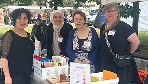 Vier Frauen stehen unter einem weißen Pavillon hinter einem Stand mit Bastelmaterial und einem Würfelspiel. Im Hintergrund hängt ein Banner mit der Aufschrift „Beirat für Menschen mit Behinderungen“.