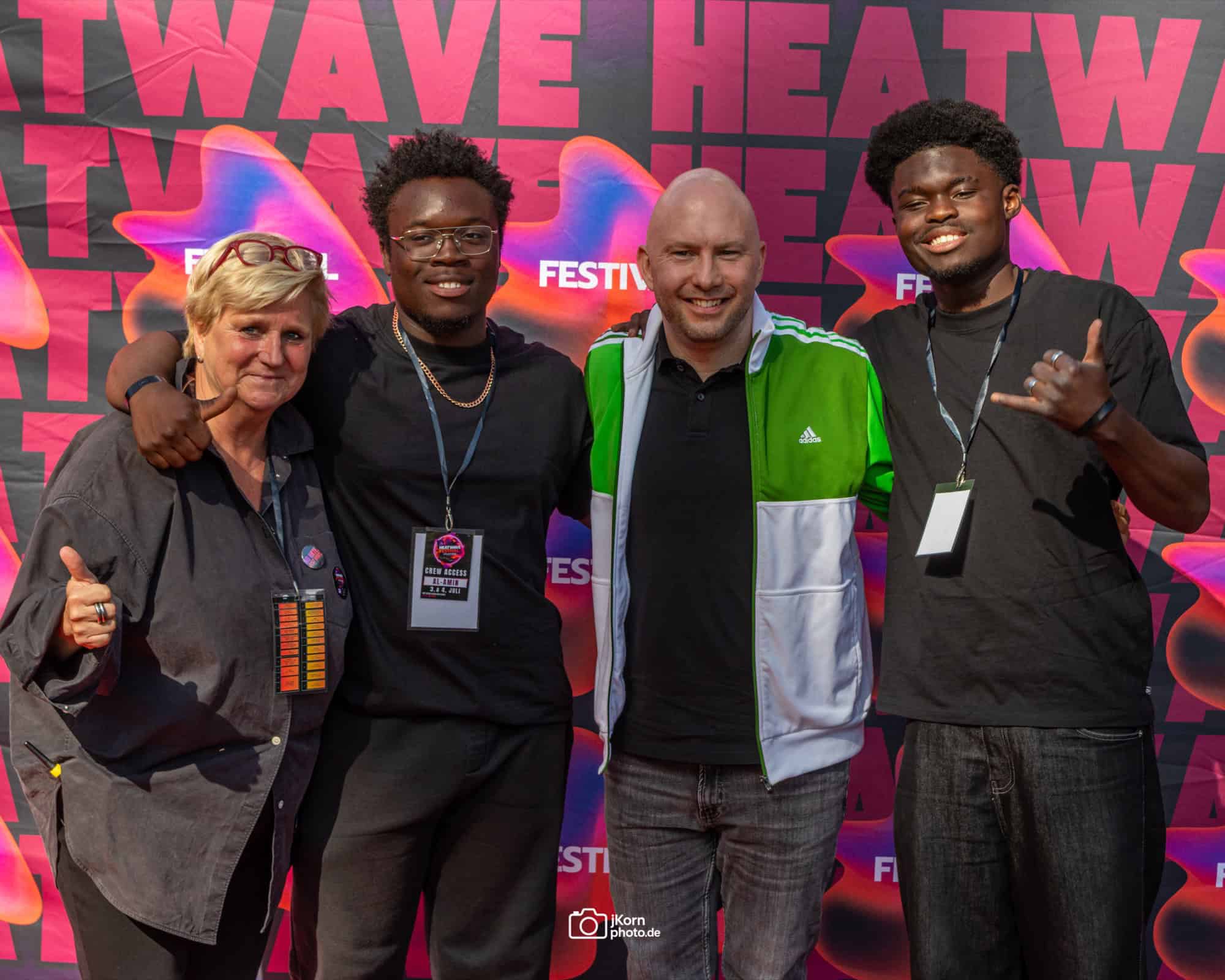 Vier Personen stehen Arm in Arm vor einer pink-bunten Fotowand mit dem Schriftzug HEATWAVE Festival und lächeln in die Kamera.