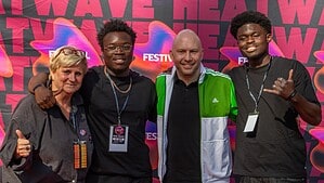Vier Personen stehen Arm in Arm vor einer pink-bunten Fotowand mit dem Schriftzug HEATWAVE Festival und lächeln in die Kamera.