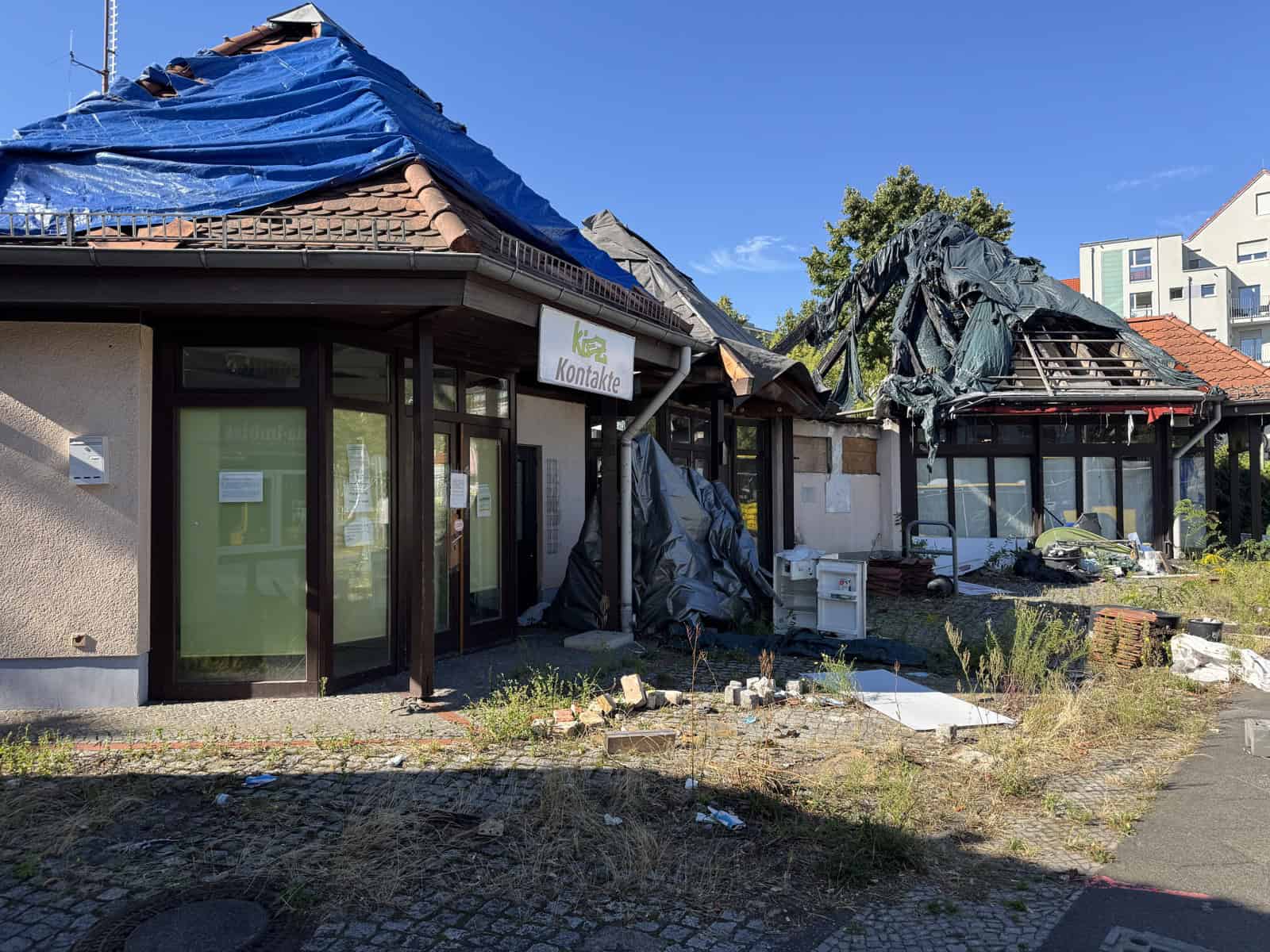 Nahaufnahme der Brandruine mit dem Schriftzug Kontakte, zerrissene Planen auf dem Dach