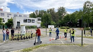 Jugendliche mit E-Scootern und Trainer üben auf einem Verkehrsübungsplatz.