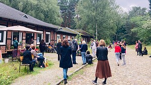 Menschen gehen und stehen auf dem gepflasterten Weg vor den Ateliergebäuden des Künstlerhofs