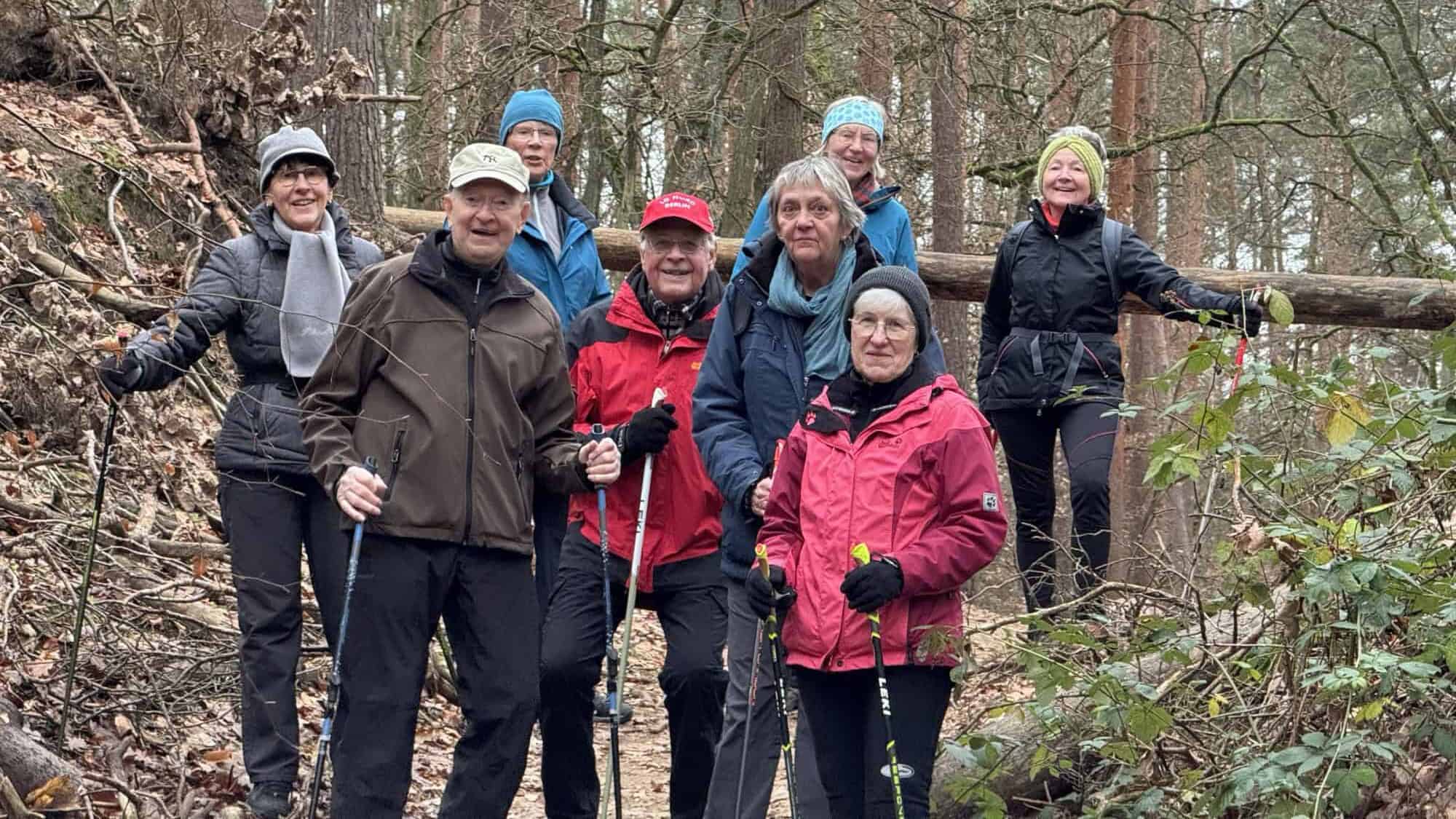 Acht Teilnehmerinnen und Teilnehmer mit Walking-Stöcken auf einem Waldweg im Tegeler Forst