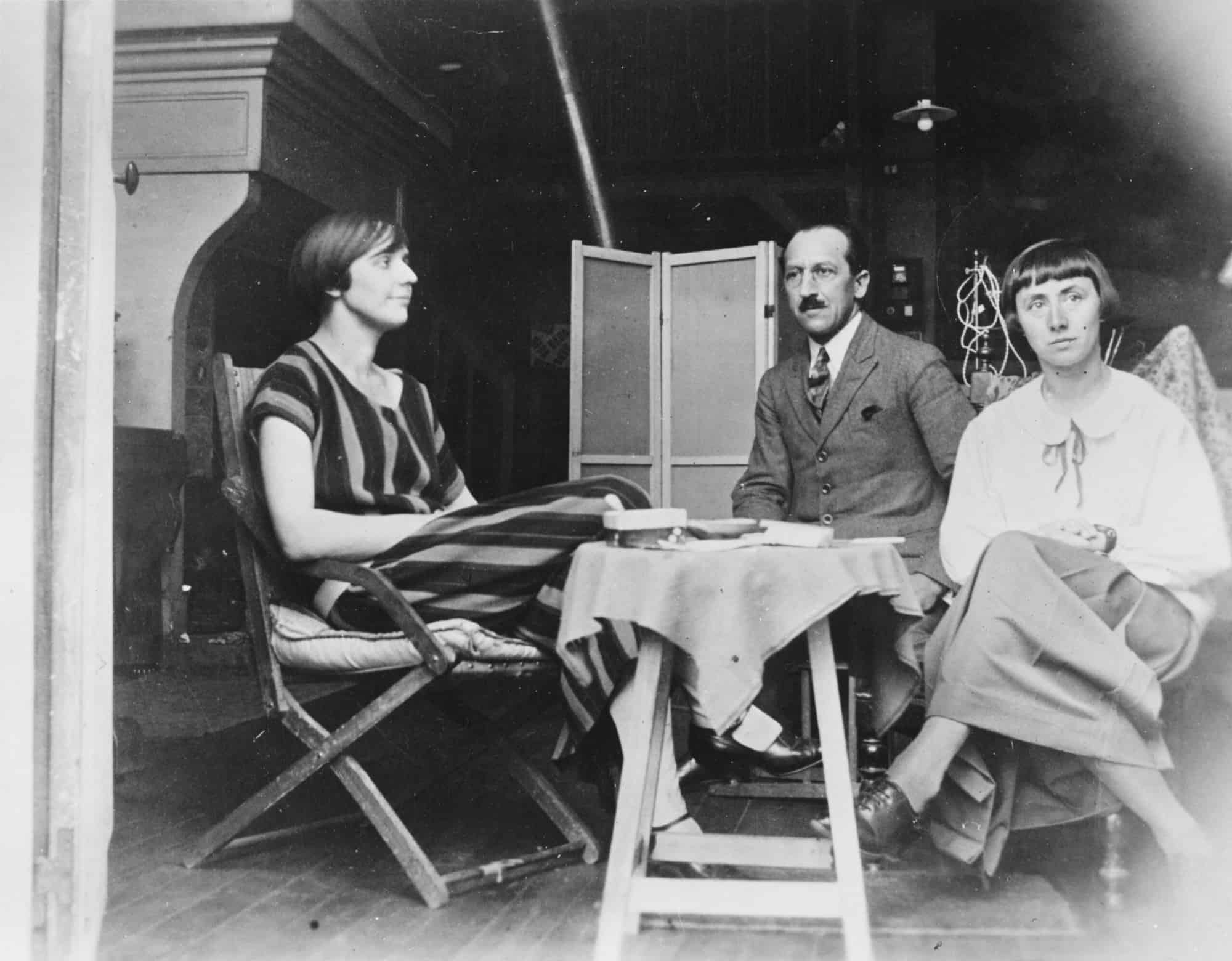 Historische Schwarzweißaufnahme: Drei Personen sitzen 1924 in einem Pariser Atelier um einen kleinen Tisch.