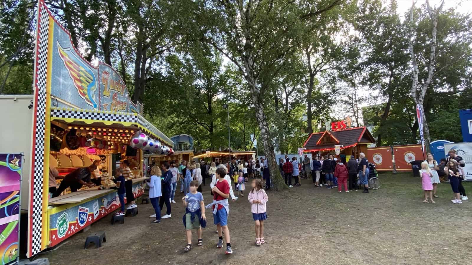 Familien mit Kindern stehen vor einem Rummelstand zum Büchsenwerfen.